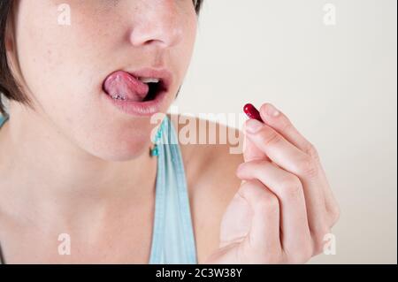 Eating Disorder Concept - Studioaufnahme eines weiblichen Models in ihren 20er Jahren, das eine Vitaminpille auf weißem Hintergrund verschluckt Stockfoto