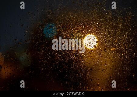 Regentropfen auf einem Fenster mit den Lichter der Stadt in der Nacht, abstrakt verschwommener Hintergrund mit farbigen Lichtern. Stockfoto
