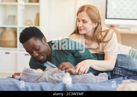 Portrait von glücklichen interracial Familie spielen mit Baby Junge, während auf dem Bett in gemütlichen Zuhause Interieur, kopieren Raum liegen Stockfoto