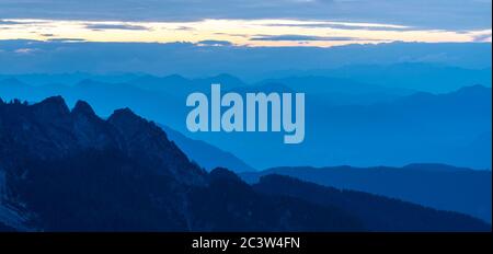Spektakuläre Aussicht auf blaue Bergketten Silhouetten und Nebel in Tälern. Die Julischen Alpen, Nationalpark Triglav, Slowenien. Blick vom Berg Slemenova Stockfoto