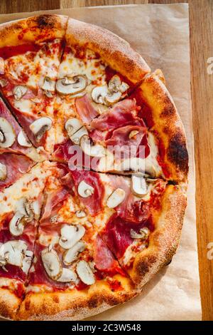 Draufsicht auf Pizza mit Prosciutto und Champignons auf Holzgrund. Stockfoto