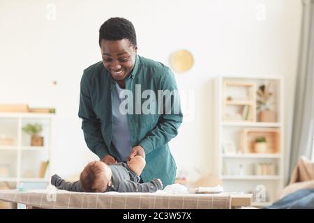 Warm-getönte Porträt von liebevollen afroamerikanischen Vater spielt mit niedlichen Baby Junge, während er auf Wickeltisch zu Hause, kopieren Raum kleiden Stockfoto