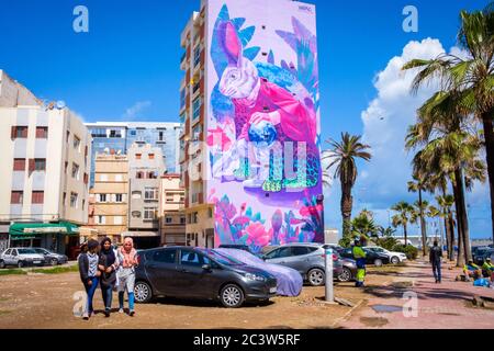 Marokko, Casablanca: Gebäude und Wandgemälde auf dem Zerktouni Boulevard. Drei Mädchen, die an Gebäuden und Wandgemälden mit einem riesigen Kaninchen vorbeigehen, Arbeit von Mexica Stockfoto