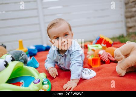 Ein schönes kaukasisches Kind im Hof spielt mit Spielzeug auf einer Decke Stockfoto