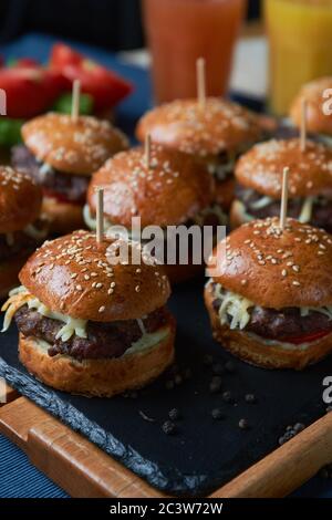 Saftige Burger mit Zwiebelringen, Gurken, Salat, Käse auf schwarzem Stein Hintergrund Stockfoto