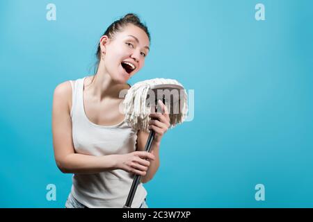 Ein junges Mädchen singt fröhlich in einem Mopp wie in ein Mikrofon. Isoliert auf blau Stockfoto