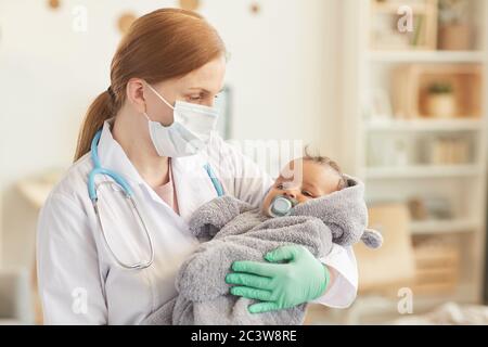 Taille up Porträt von weiblichen Arzt hält niedlich Mixed-Race Baby während der Überprüfung in Haus-Interieur, kopieren Raum Stockfoto