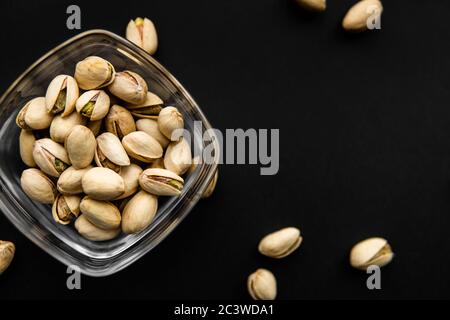 Pistazien in einem kleinen Teller mit verstreuten Nüssen von Mandeln um einen Teller auf einer schwarzen Oberfläche. Pistazie ist ein gesundes vegetarisches Protein nahrhaft Stockfoto