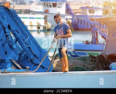 San Pedro del Pinatar, Murcia, Spanien, 22. Juni 2020: Ein Besatzungsmitarbeiter an Bord eines Fischerbootes oder Schiffes, der die Seile für den Hafen vorbereitet Stockfoto