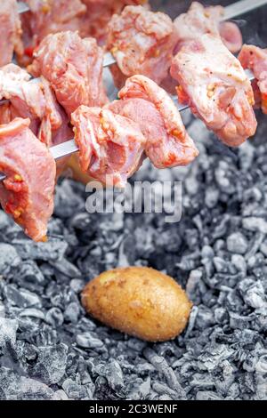 Hände des Menschen bereitet Grillfleisch mit Kartoffeln auf Spieß vom Grill auf Feuer im Freien. Konzept der Lifestyle rustikale Zubereitung von Speisen Stockfoto