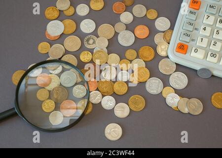 Münzen verschiedener Länder, Taschenrechner und Lupe vor dunklem Hintergrund. Stockfoto