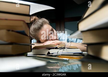 Vorbereitung auf den Hochschulzugang. Das Mädchen schlief auf dem Stapel der geöffneten Bücher ein Stockfoto