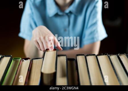 Mädchen nimmt ein Buch aus einer Reihe von Büchern, Nahaufnahme einer Hand, selektiver Fokus Stockfoto