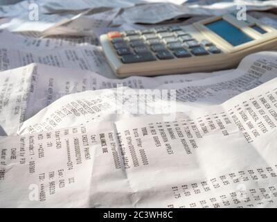 Ein Haufen von Einkaufsscheinen / Rechnungen mit aufgegliederten britischen Sterling Supermarkt Käufe an der Vorderseite in scharfem Fokus, mit einem Rechner auf der Oberseite hinter. Stockfoto