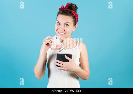 Eine junge Frau setzt oder nimmt glücklich aus einem Box für Einsparungen eine neue Rechnung von zehn Euro Stockfoto