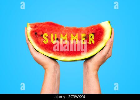 Wassermelone Scheibe mit dem Text Sommer. Die Hand einer Frau hält ein Stück Wassermelone auf blauem Hintergrund. Sommerurlaub Konzept, Unterhaltung und Stockfoto