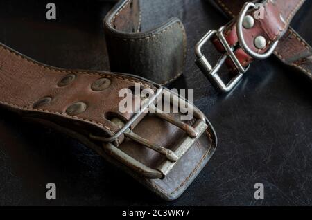 Fragment von zwei alten echten Lederhalsbändern auf einem dunklen Tisch. Zerbrochene, schäbige Leder- und Metallbeschläge. Echte Vintage Hundehalsbänder. Liebe zu den Tieren. Stockfoto