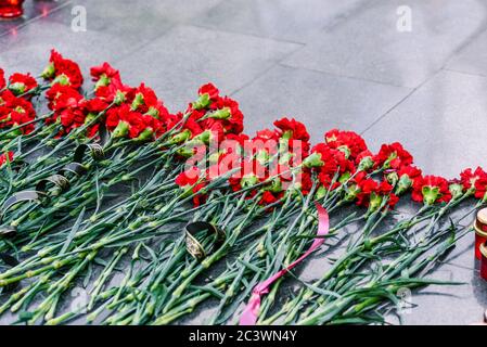 Rote Nelken auf einer Marmorplatte. Symbol der Trauer, Blumenauflegung an der Gedenkstätte Stockfoto