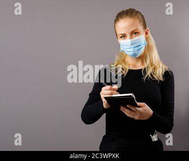 Junge blonde Kellnerin nimmt Aufträge in einer chirurgischen Maske Stockfoto