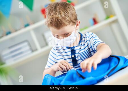 Liebenswert kleinen Jungen im Kindergarten mit Maske auf wegen Coronavirus Pandemie Stockfoto