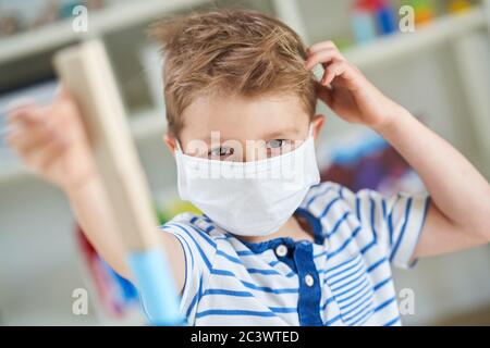 Liebenswert kleinen Jungen im Kindergarten mit Maske auf wegen Coronavirus Pandemie Stockfoto