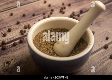 Piment in einem Keramikmörtel und verstreut Piment auf einem Holztisch. Nahaufnahme Stockfoto