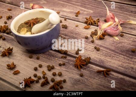 Piment in einem Keramikmörtel und verstreute Knoblauchzehen, Sternanis und Piment auf einem Holztisch. Nahaufnahme Stockfoto