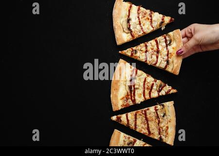 Eine Frau nimmt ein Stück Pizza. Dunkler Hintergrund. Draufsicht Stockfoto