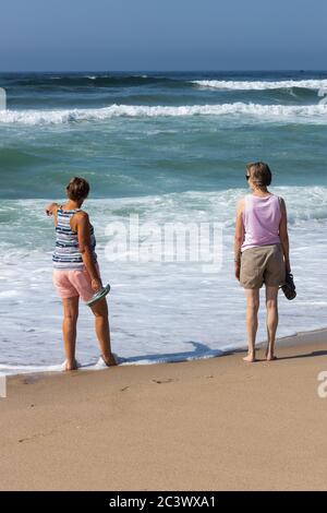 Zwei entspannt aussehende ältere Frau am Strand, die am Ufer mit weißen Wellen herumläuft. Portugal Stockfoto