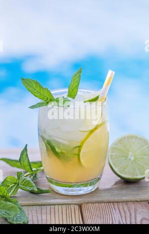 Ein frischer Mojito Drink mit Minzblättern und Limette und zerkleinerten Eis, mit blauem Wasser im Pool entkokend im Hintergrund. Platz für Text über d kopieren Stockfoto