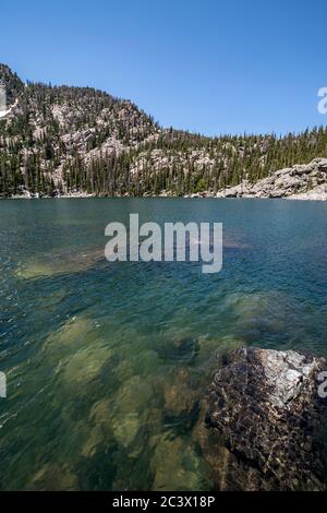 Lake Haiyaha im Rocky Mountain National Park während des Mittags mit untergetauchten Felsen und Farben, entfernten Bergen und einem dramatischen Himmel Stockfoto