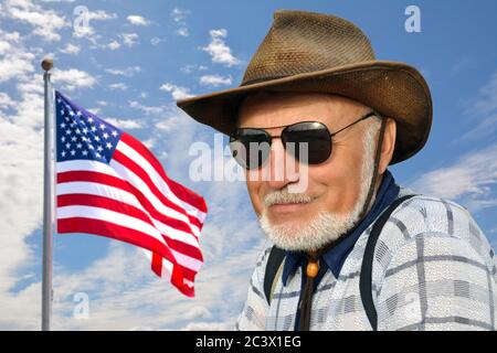 Ein amerikanischer Cowboy steht vor einem blauen Himmel mit einer sich entwickelnden amerikanischen Flagge. Er trägt einen Strohhut und eine Brille. Elemente davon Stockfoto