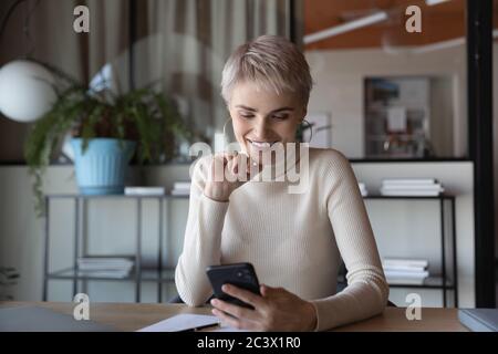 Büroangestellte sitzt am Schreibtisch und hat mit dem Smartphone Pause gemacht Stockfoto