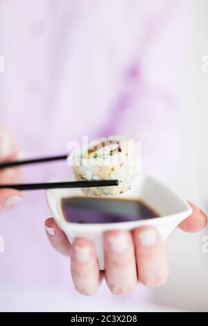 Nahaufnahme der Frau hält Schüssel mit Sojasoße und Essstäbchen mit Sushi-Rolle, japanisch traditionelle gesunde Mahlzeit Konzept. Stockfoto