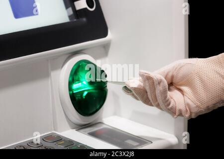 Frau legt eine Bankkarte in den ATM-Empfänger ein. Weibliche Hand im Schutzhandschuh, finanzielle Transaktionen und Sicherheitsmaßnahmen während der covid-19 Stockfoto