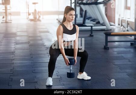 Starke junge Frau tut Kniebeugen mit Hantel im Sportverein Stockfoto