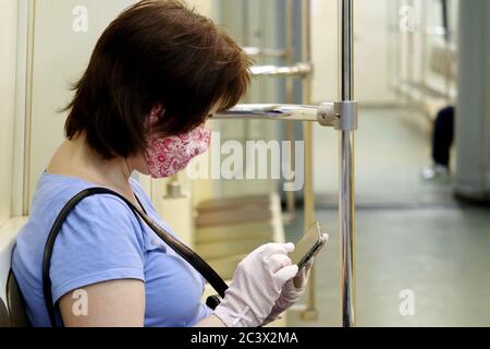 Frau in Maske und Schutzhandschuhe sitzen in einem U-Bahn-Zug mit Smartphone. Innenraum der U-Bahn-Auto während covid-19 Coronavirus Pandemie Stockfoto