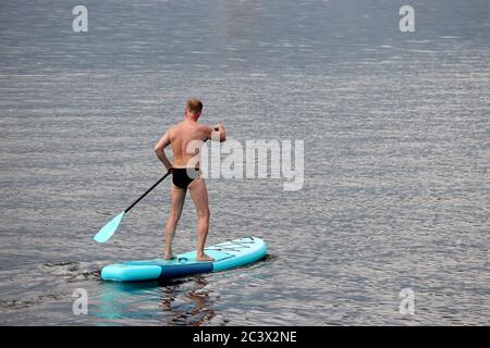 SUP Surfen, Mann in Badehose stehend mit Paddel auf einem Brett im Wasser. Paddelboarding im Sommer Stockfoto