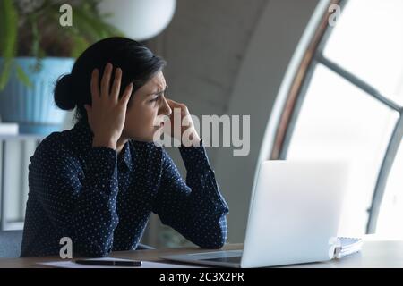 Überarbeiteter indischer Mitarbeiter, der am Arbeitsplatz sitzt und Kopfschmerzen hat Stockfoto