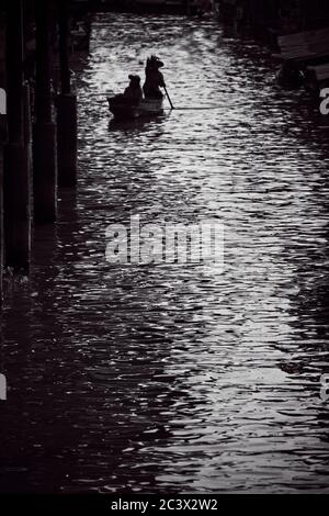 Bangkok schwimmenden Markt Mono Prozess Einzelboot in der Ferne mit Zwei Menschen silhouetted gegen Highlight im Wasser Stockfoto