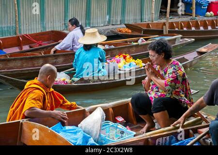 Bhudist Mönche und Einheimische in Bangkoks schwimmenden Markt Gruppe von Menschen in Booten interagieren miteinander Mönch unten links Im Vordergrund Stockfoto