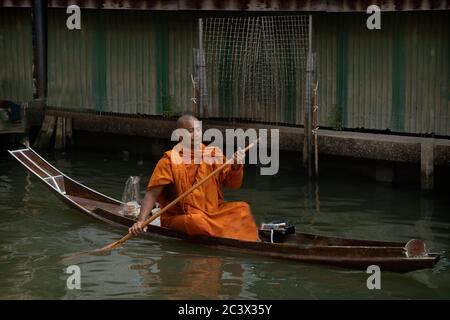 Bhudist Mönche und Einheimische auf Bangkok schwimmenden Markt. Ein Mönch paddelt traditionelles Boot, das sich von links nach rechts bewegt Stockfoto