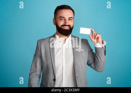 Portrait des fröhlichen Unternehmers zeigt Visitenkarte mit leerem Raum für Design vor blauem Hintergrund Stockfoto