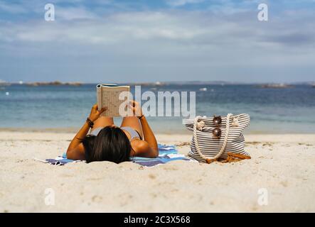 Gebräunte Frau Lesen und genießen am Strand am Meer Stockfoto