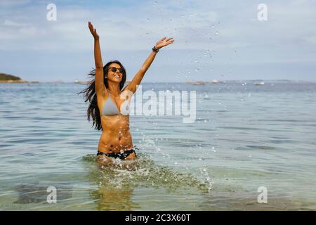 Gebräunte Frau, die Wasser in die Luft am Strand wirft und den Sommer genießt Stockfoto