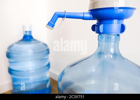 Sauberes Wasser zu Hause trinken. Nahaufnahme des großen blauen Pumpenkühler-Flaschenmechanismus für Haus oder Büro. Lieferung mit zwei Flaschen Stockfoto