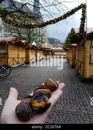 Nahaufnahme einer Handvoll traditioneller Leckerbissen - einer gerösteten Kastanie. Leere Straße mit geschlossenen Weihnachtsmarkt Ständen. Festliche Stimmung im Freien Stockfoto