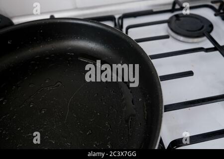 Ölige schmutzige schwarze Bratpfanne auf einem Gasherd gelassen. Ungewaschene, schmutzige Kochgeschirr nach dem Kochen. Ungesunde Lebensmittel und Lebensstil, die zu Fettleibigkeit führt. Stockfoto