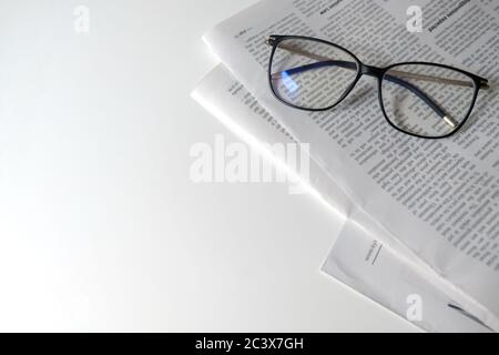 Zeitung in Isolation lesen. Lernort für Heimunterricht oder Arbeitsplatz für einen Freiberufler. Zeitung und Brille auf weißem Schreibtisch, leerer Raum Stockfoto