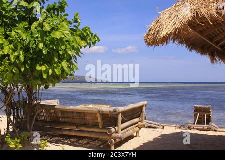 Tropischer Strohschirm und Sofas mit Kissen an der Strandbar am sonnigen exotischen Strand mit Blick auf Ebbe Ozean in Gili Air Island, Lombok, Indonesien Stockfoto